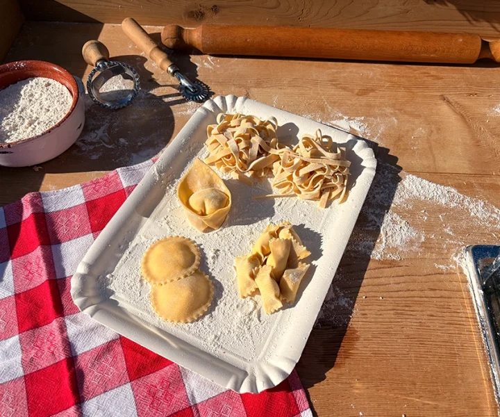 Mani impastano pasta fresca, farina sul tagliere, sorriso.